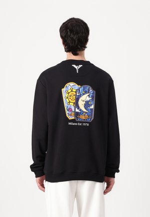 Schwarzer Pullover mit buntem Grafikdesign auf der Rückseite, das Sonnen- und Mondmotive zeigt. Darunter der Text "Milano Est 1978". Weicher Stoff.