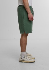Shorts en mélange de coton vert avec une taille élastique, des poches latérales et un ourlet légèrement incurvé. Associés à des baskets blanches et des chaussettes.