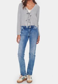 Grå ribbad kort topp med v-ringning och snörning, kombinerad med ljusblå raka jeans och beige sneakers med gröna ränder.