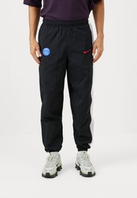 Sorte nylon trackbukser med elastisk talje, prydet med et blåt PSG-logo og et rødt Nike swoosh. Inkluderer hvide sideaccenter.