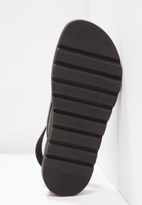 Semelle de sandale noire avec des rainures horizontales, surface texturée et bords arrondis. Pas de marque visible ni d'accents notables.
