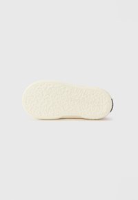 Hvit gummisåle til sneakers med teksturert grep mønster og buede kanter, har en liten svart detalj nær hælen.
