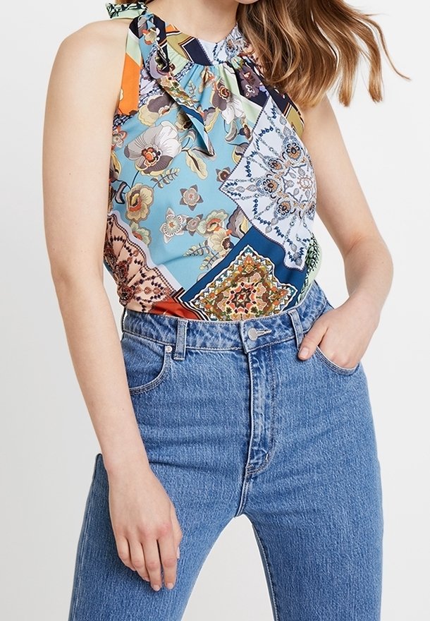 Top a scollo all'americana multicolore con motivi floreali e geometrici, completo di un fiocco al collo. Abbinato a jeans blu a vita alta.