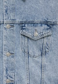 Tissu en denim bleu clair avec des coutures verticales, des boutons-pression argentés et une poche à rabat pointu avec fermeture par bouton.