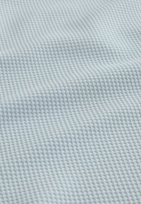 Tissu gris clair avec un petit motif diamant texturé et des ombres subtiles créant de douces ondulations à la surface.