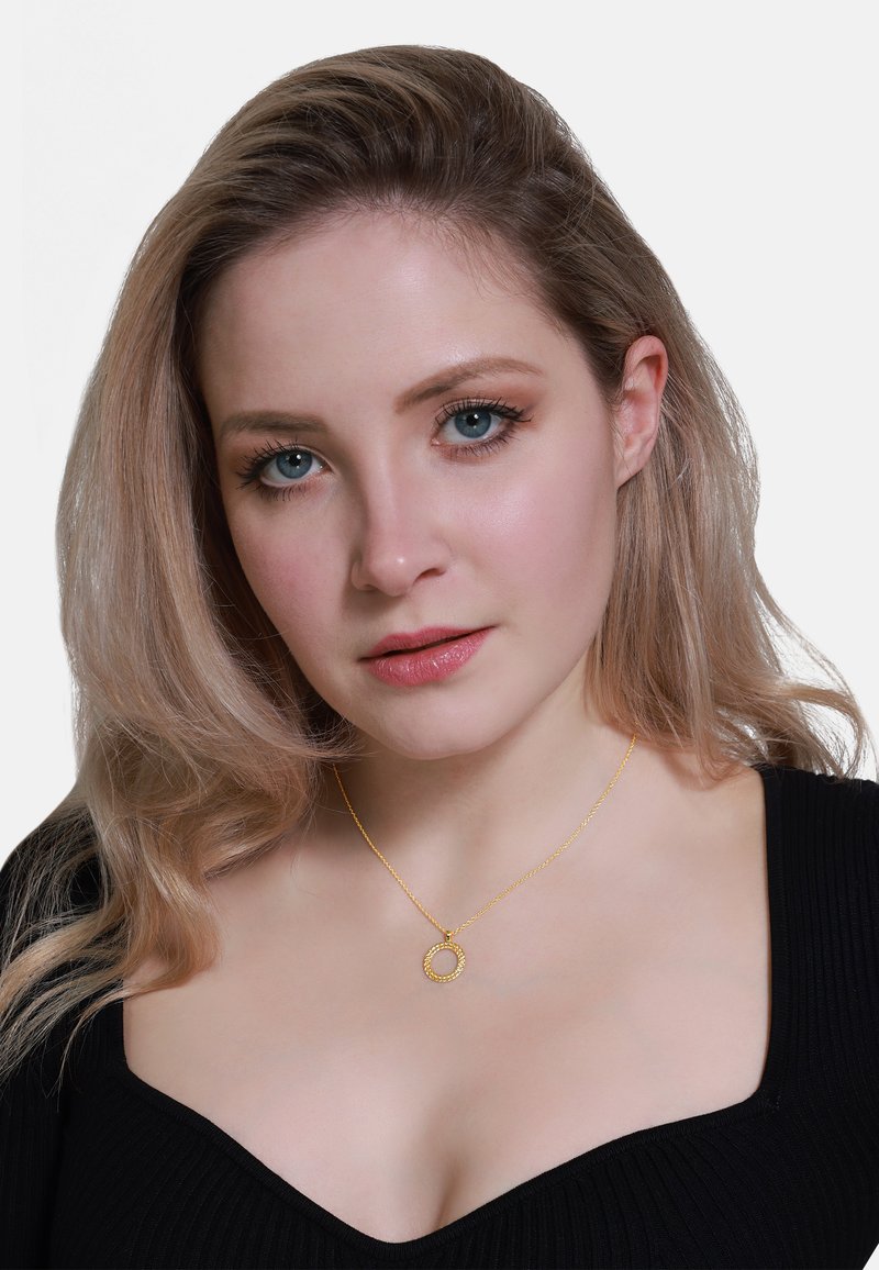 Gouden hanger ketting met een ronde vorm en een korrelige textuur, hangend aan een delicate ketting. Draagt bij een zwarte ribbeltop.