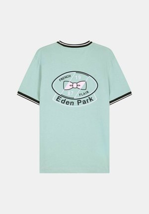 T-shirt vert clair à manches courtes avec col et poignets rayés noirs et blancs, ornés d'un nœud rose et du texte « Eden Park » au dos.
