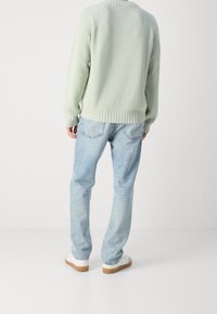 Maglione verde chiaro a righe con maniche lunghe, abbinato a jeans dritti blu chiaro e sneakers bianche con suole color nocciola.