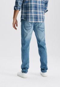 Jasnoniebieskie dżinsy o prostym kroju, z tylnymi kieszeniami i subtelnymi detalami przeszycia. Zestawione z niebieską koszulą w kratę i białymi trampkami.