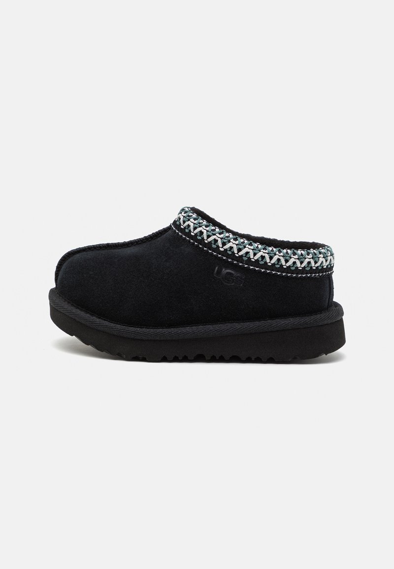 Zapato negro de ante tipo slip-on con una suela texturizada y un pespunte decorativo multicolor alrededor del cuello. Cuenta con el logo de UGG en el lateral.