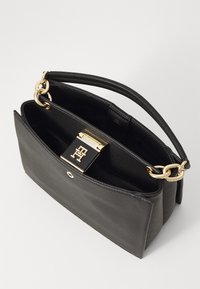 Black leather handbag with a structured shape, gold chain handle, and a decorative clasp featuring a logo. Interior is open and lined.