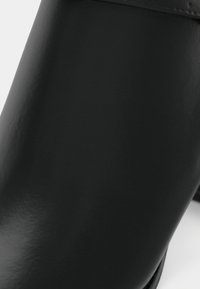 Must mustaankle saapad, millel on sile ja läikiv pind ning minimalistlik disain. Omab ümarat varbaosa ja peent õmblust õmbluste ääres.