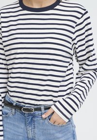 Chemise à manches longues à rayures horizontales bleu marine et blanches, col rond et coupe décontractée. Assortie à un jean en denim bleu et une ceinture noire.