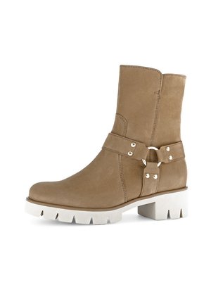 Helle Wildleder-Ankle-Boots mit einer weißen, klobigen Sohle, die seitlich mit einem dekorativen Riemen und einer Schnalle versehen sind, um zusätzliche Textur zu bieten.