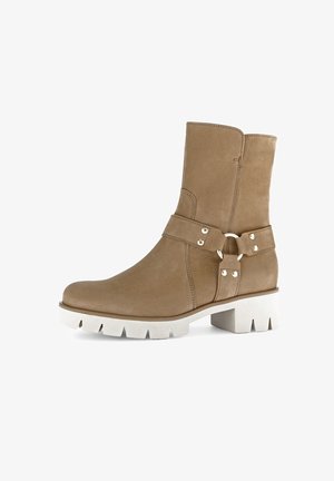 Tan suede ankle boot with a white chunky sole, featuring a decorative strap and buckle detail on the side for added texture.