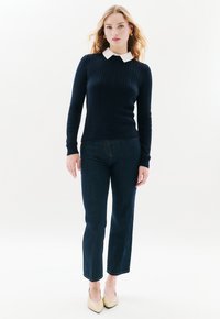 Marineblauer Strickpullover mit strukturiertem Muster, weißem Kragen, kombiniert mit dunklen Denim-Jeans und beigen spitzen Ballerinas. Saubere, enganliegende Silhouette.