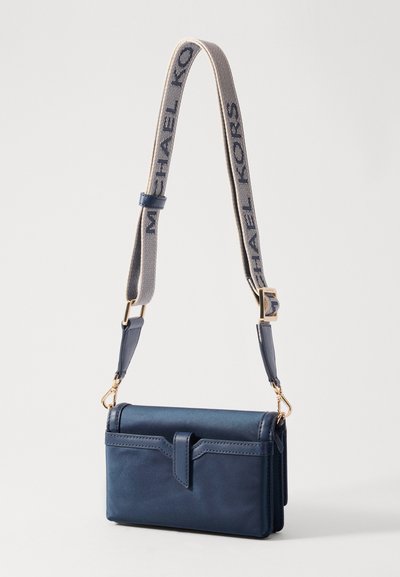 Sac en cuir marine à bandoulière avec un rabat, quincaillerie dorée et une sangle beige portant l'inscription "MICHAEL KORS" en texte marine.