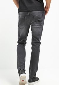 Mäns slim-fit jeans i mörkgrå denim, med en blekt finish, bakfickor med vinkelställd sömnad och slitna kanter vid fållen.