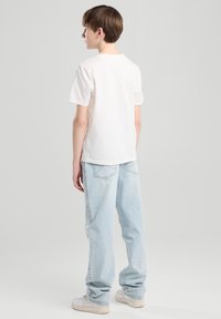 Valkoinen puuvillapaita, lyhyet hihat, rento malli. Yhdistetty vaaleansinisiin yli-isoihin farkkuihin ja valkoisiin urheilukenkään.