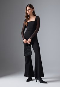 Mono negro con escote cuadrado y mangas largas de tul, combinado con un pequeño bolso negro texturizado y tacones de punta.