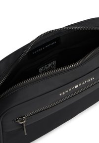 Μαύρο φερμουάρ τσαντάκι Tommy Hilfiger με μπροστινή τσέπη, ανοιχτό κύριο διαμέρισμα που δείχνει την εσωτερική ετικέτα και έναν κωδικό QR στο εσωτερικό.