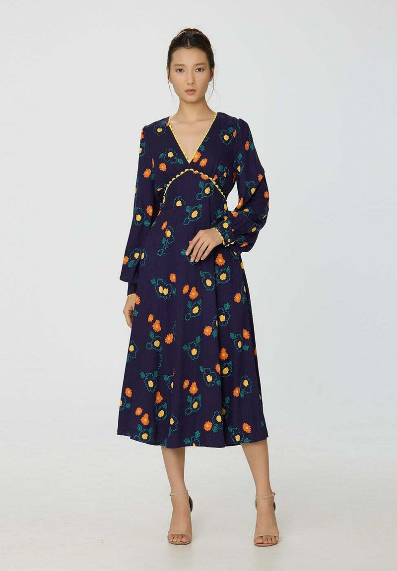 Robe longue bleu marine à imprimé floral orange et vert, décolleté en V, manches longues et détail de taille froncée. Texture lisse, longueur mi-mollet.