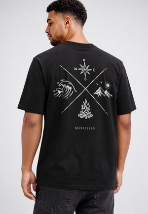 Man wearing black t-shirt with crossed arrows on back, featuring compass, ocean wave, campfire, and mountain with sun icons.