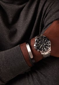 Stainless steel watch with black dial, silver accents, and chronograph features. Paired with a black braided bracelet with metal clasp.