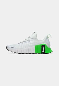 White athletic shoe with textured upper, green accent on the heel, black sole, and reflective details. Laced design with a pull tab.