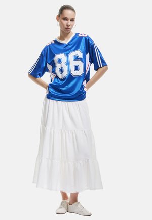 Jersey en satin bleu avec des accents blancs et rouges, portant le numéro "86" à l'avant, assorti d'une jupe blanche à volants et de baskets légères.