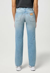 Heledad sinine denim, sirge lõikega teksad, millel on kaks tagakotti, pruun nahatäkk ja tuhm tekstuur.