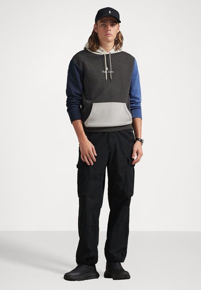 Sweatshirt com capuz de corpo cinza, mangas azuis e um bolso frontal, combinado com calças cargo pretas e ténis escuros. Ajuste e design casuais.