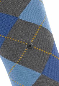 Calzini argyle grigi e blu con cuciture gialle, caratterizzati da un logo nero rotondo al centro; realizzati in tessuto a maglia.