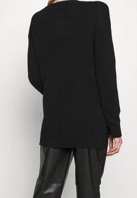 Schwarzer Strickpullover mit lässiger Passform, geripptem Saum und langen Ärmeln. Geschmeidige Textur, einfaches Design und seitliche Schlitze am Saum.