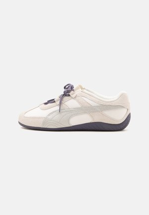 Λευκό και μπεζ χαμηλό sneaker με σκούρα γκρι κορδόνια και σόλα, σουέτ λεπτομέρειες και λείο, καμπυλωτό σχέδιο σε μονόχρωμο φόντο.