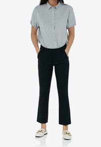 Jasnoszara krótko rękawowa koszula z guzikami, czarne dopasowane spodnie i białe loafersy z złotymi elementami. Prosty i dopasowany fason.