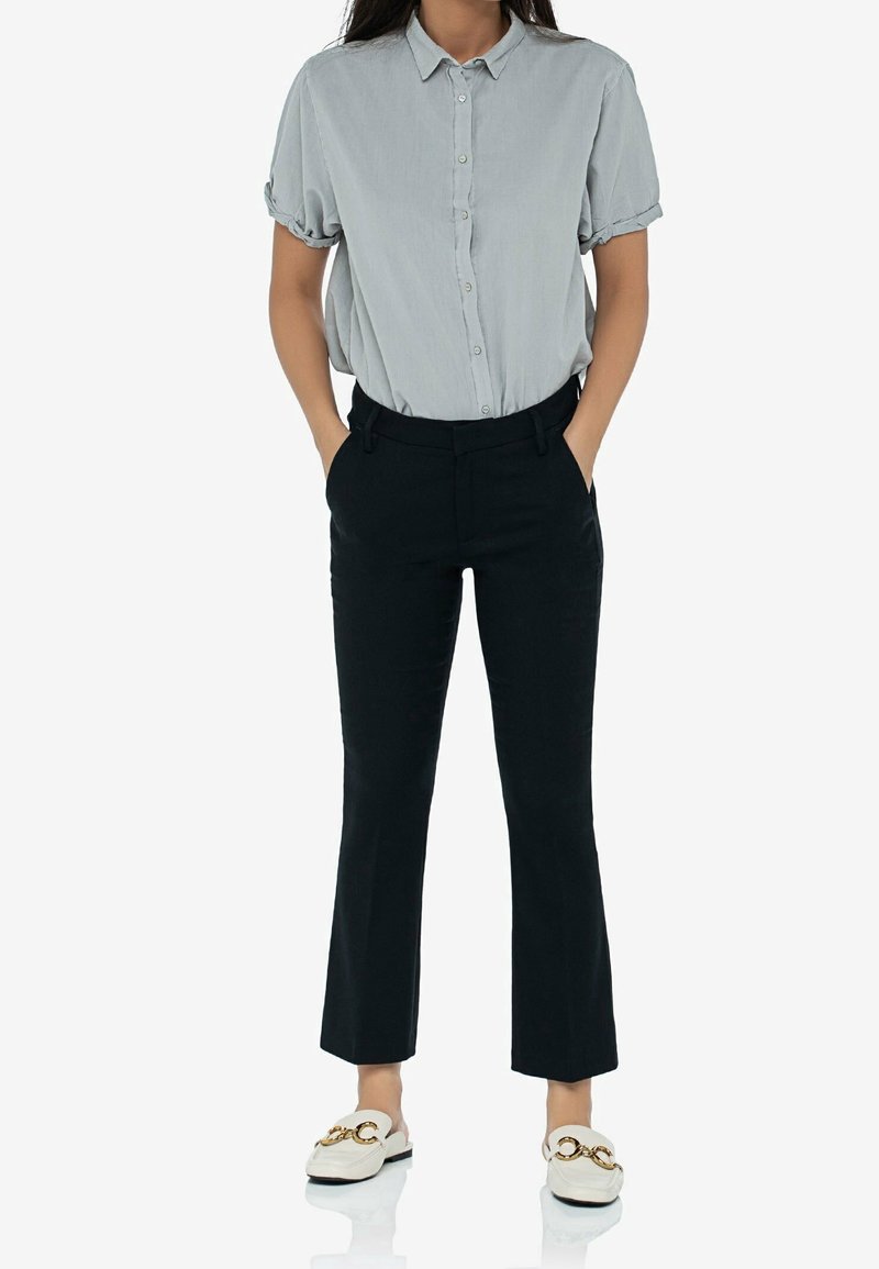 Jasnoszara krótko rękawowa koszula z guzikami, czarne dopasowane spodnie i białe loafersy z złotymi elementami. Prosty i dopasowany fason.