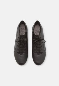 Zapatillas deportivas negras con un diseño elegante, material sintético suave, acentos texturizados y un sistema de cordones tradicional.