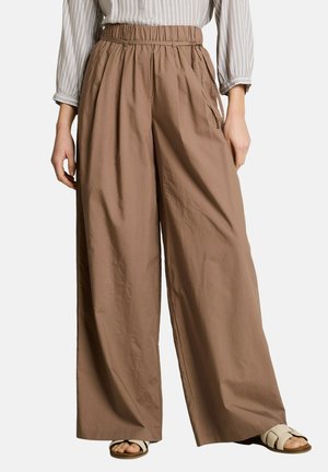 Woman wearing loose, high-waisted brown wide-leg pants with side pockets, a striped long-sleeve shirt, and white flat sandals.