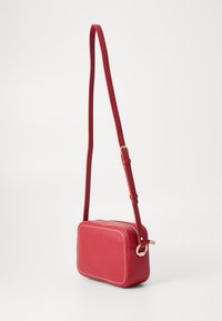 Borsa a tracolla in ecopelle rossa dalla forma rettangolare arrotondata, con ferramenta dorata e cuciture bianche a contrasto sui bordi. Inclusa tracolla regolabile.