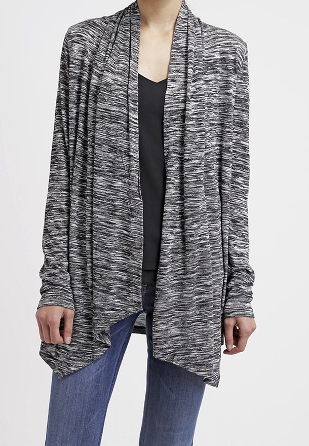 Femme portant un cardigan gris et noir chiné à manches longues et ouvert sur le devant, par-dessus un haut noir à col en V et un jean bleu.