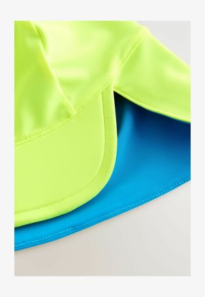 Neon sárga és kék szövet sapka sima, fényes textúrával. Ívelt karimával és réteges dizájnnal rendelkezik, amely a kontrasztos színeket mutatja be.