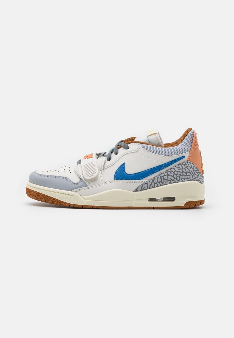 Baskets basses blanches avec logo Nike bleu, détails imprimé éléphant gris, semelle et talon marron, lacets gris et détails orange.