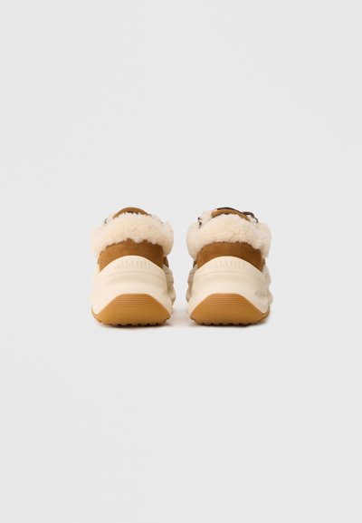 Et par tan- og hvide sneakers med fluffy cremegulv, set fra bagsiden på en simpel lys baggrund.