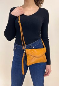 Geel leren schoudertas met een geometrisch klepdesign, voorzien van een zilveren rits en een verstelbare schouderband.