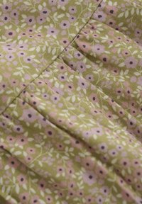 Grön tyg med ett blommönster som har rosa och lavendelfärgade blommor, accentuerade av svarta centra och känsliga gröna blad. Texturerad yta.