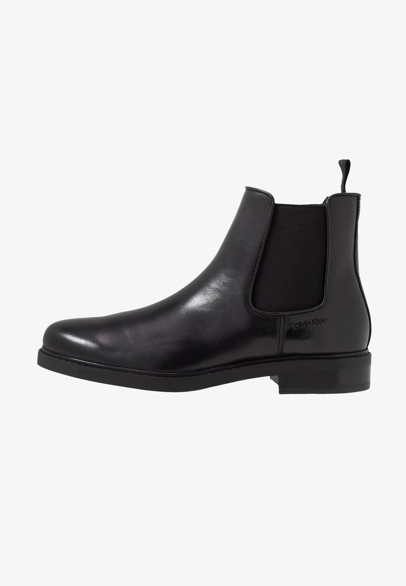 Bottine Chelsea en cuir noir avec panneau latéral élastique et languette, talon bas, design épuré et logo Calvin Klein embossé près de la cheville.