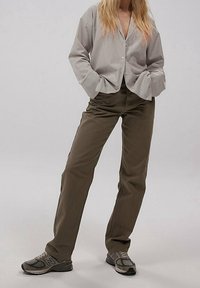 Blouse grise à rayures avec manches larges, boutonnée ; associée à un pantalon droit vert olive et des chaussures de sport grises.