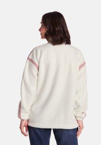 Cream fleece pullover with long sleeves, featuring soft texture and light pink accents on the shoulders, designed for a relaxed fit.