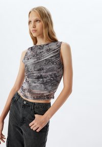 Top ajustado y corto en una tela translúcida y texturizada con un estampado de serpiente en tonos de gris y negro. Presenta un cuello alto y un diseño sin mangas.